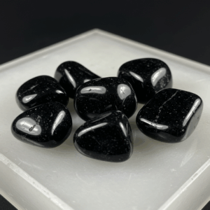 Polished tumbled Black Obsidian natural volcanic glass on white matte background, healing crystal stones.
